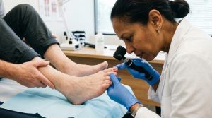 Dermatologista examinando a unha do pé de um paciente com dermatoscópio em um consultório moderno.