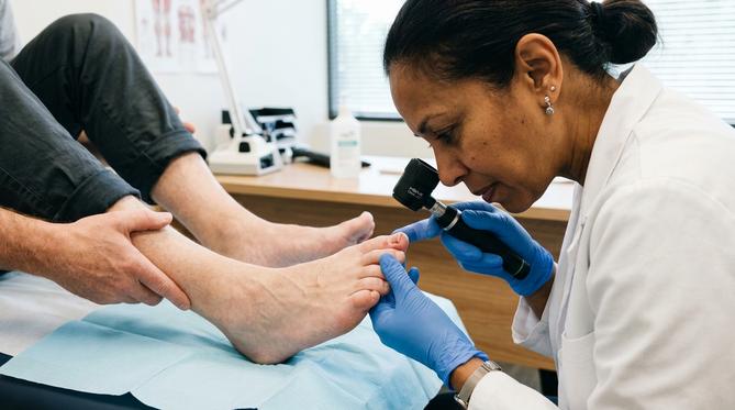 Dermatologista examinando a unha do pé de um paciente com dermatoscópio em um consultório moderno.